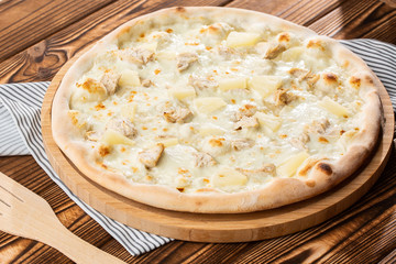 Pizza topped with sauce, chicken, cheese and pineapple serve on wooden plate on wooden table. Photo of Hawaiian pizza. 