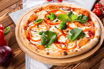 Vegetarian pizza on a wooden background with mushrooms, broccoli, cheese and sweet pepper and basil. Top view.