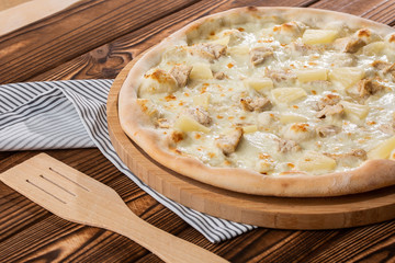 Pizza topped with sauce, chicken, cheese and pineapple serve on wooden plate on wooden table. Photo of Hawaiian pizza. 