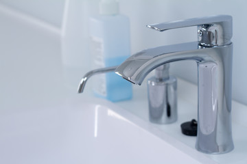 A modern water tap sink with faucet in minimalistic style and built-in soap dispenser in expensive loft bathroom, soft focus
