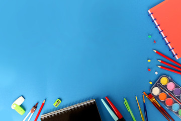 School various color stationery, paints, pencils, pens, on a blue background. Back to school concept, top view, copy space