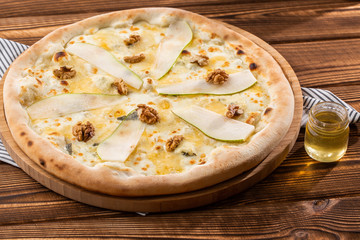 Traditional pizza with pear, nuts and blue cheese on a wooden background. Close up. Top view.