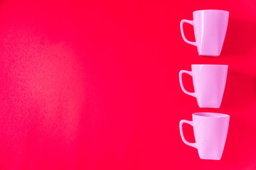 3 pink winter coffee cup mugs lined up in a row for a break time meeting; Copyspace with empty room space for copy text on red horizontal background; Girlie female valentines theme.