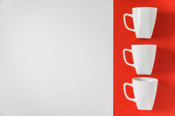 3 white winter coffee cup mugs lined up in a row for a break time meeting; Copyspace with empty room space for copy text on red horizontal background; Christmas holiday or Valentines.