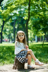 Beautiful little girl sitting in the park on a bright sunny summer day.