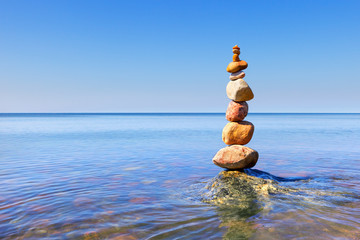 Rock zen pyramid of colorful pebbles standing in the water on the background of the sea