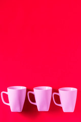 3 pink winter coffee cup mugs lined up in a row for a break time meeting; Copyspace with empty room space for copy text on red vertical background; Girlie female valentines theme.