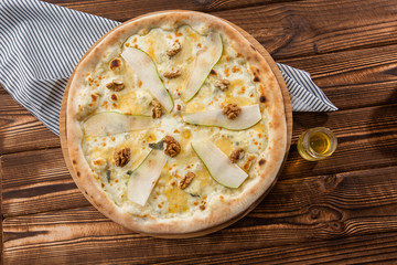 Traditional pizza with pear, nuts and blue cheese on a wooden background. Close up. Top view.