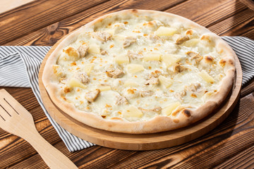 Pizza topped with sauce, chicken, cheese and pineapple serve on wooden plate on wooden table. Photo of Hawaiian pizza. 