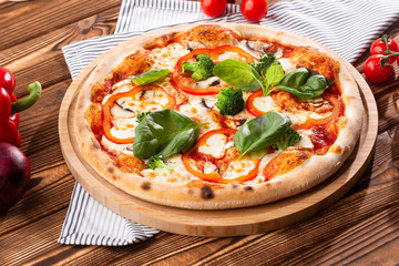 Vegetarian pizza on a wooden background with mushrooms, broccoli, cheese and sweet pepper and basil. Top view.