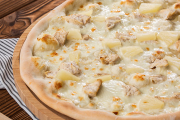 Pizza topped with sauce, chicken, cheese and pineapple serve on wooden plate on wooden table. Photo of Hawaiian pizza. 