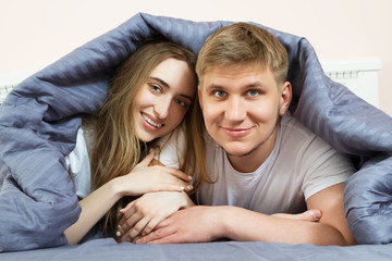 Cute loving couple is lying on the bed in the bedroom in the morning. Young happy couple lying in bed and smile