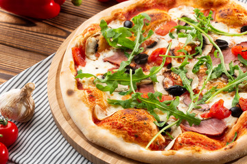 Pizza with ham , arugula (salad rocket), rucola, mushrooms olives and mozzarella  on  wooden background close up. Italian cuisine.