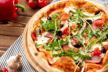 Pizza with ham , arugula (salad rocket), rucola, mushrooms olives and mozzarella  on  wooden background close up. Italian cuisine.