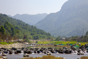 Mountain river in Sichuan, China. Reflection of the mountain in the watery surface, large river with rocks and small waterfall. 