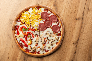 Delicious italian pizza with meat, vegetables  cheese 4 seasons isolated on wooden background. Quattro Stagioni pizza with mozzarella, ham, bacon, mushrooms, salami, mozzarella, corn, sweet pepper . 