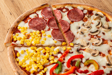 Delicious italian pizza with meat, vegetables  cheese 4 seasons isolated on wooden background. Quattro Stagioni pizza with mozzarella, ham, bacon, mushrooms, salami, mozzarella, corn, sweet pepper . 