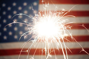 Lit sparkler burning in front of American Flag
