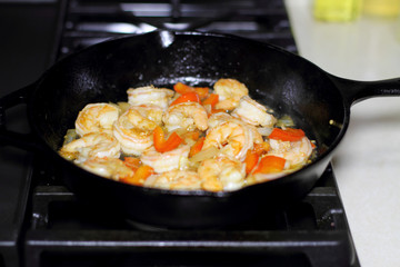 Shrimp cooking with red bell peppers and onion in a cast iron skillet on the stove.