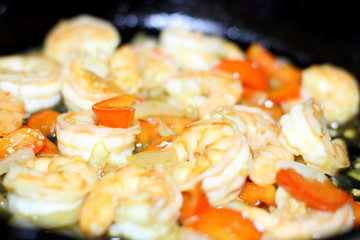 Plate of shrimp cooked with red bell peppers and onions, with slices of lemon.