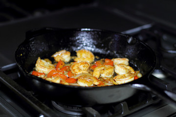 Shrimp cooking with red bell peppers and onion in a cast iron skillet on the stove.