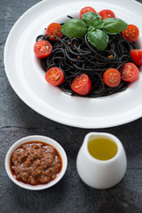 Spaghetti with squid-ink, pesto sauce, cherry tomatoes and green basil leaves served in a white plate, close-up