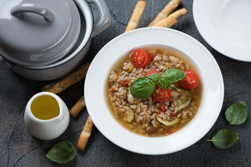 Italian spelt and minestrone soup, high angle view over grey stone background, horizontal shot