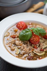 Closeup of a white plate with spelt and vegetable soup, selective focus, vertical shot