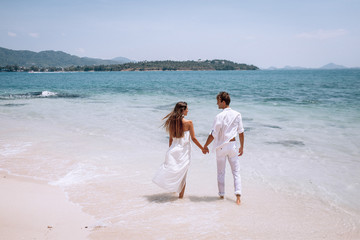 embracing romantic couplein white clothes looking on the sea on the Beautiful tropical beach vacation. Sea landscape with thai boat. Phuket. Thailand. Back view.