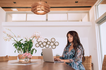 Sexy young brunette girl has a European appearance, long dark hair, smooth skin opened a laptop for work. Loft interior