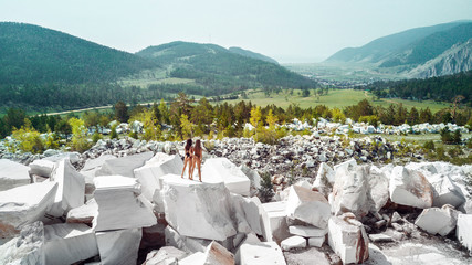 Fashion  aerial photo of Two Young, sexy women in bikini standing on the big white rocks near the wild forest and mountains. Tourism and vacation concept