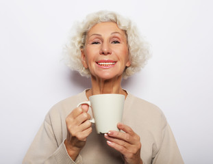 old excited lady smiling laughing, holding cup drinking coffee, tea, over white background