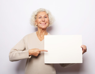 Aged woman with blank advertising board or copy space. Portrait of handsome expressive grandmother...