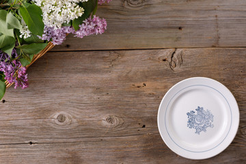 Fototapeta na wymiar Plate and decor of flowers on the background of vintage wooden planks.Vintage background with lilac flowers and place under the text. View from above. Flat lay. Cutlery.