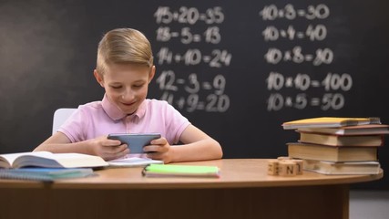 Lazy schoolboy playing videogames on phone instead of preparing task, gadget - Powered by Adobe