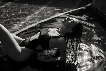 A sexy young girl in a seductive swimsuit is depicted in a black and white photo.  Fashion  Lady with Sports figure  lying on the background of an open summer pool