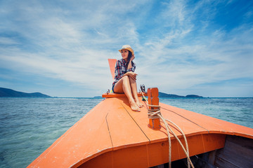Attractive young woman wearing clothes on western style sitting on the edge of a boat, refreshing...