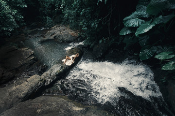 Portrait of the young Caucasian woman enjoying in front of a waterfall in an  white evening dress