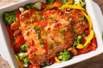 Spicy baked salmon fillet with vegetables and herbs close-up in a baking dish. horizontal top view