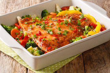 Close up of baked salmon with pepper, broccoli, cauliflower and carrot in a baking dish. horizontal