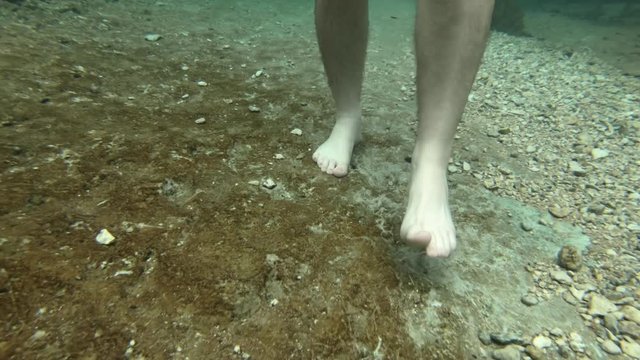 Man feet walking on slippery riverbed, underwater shot 