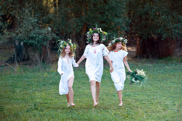 Naklejka na ściany i meble Three girls with wreaths of flowers in their hands. Midsummer. Earth Day.