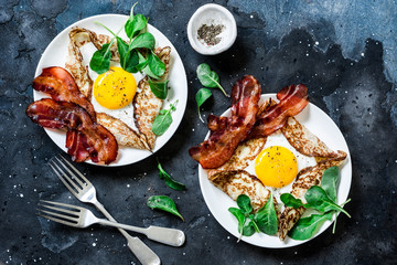 Stuffed egg crepes with bacon and arugula - delicious nutritious brunch on a dark background, top view. Flat lay - obrazy, fototapety, plakaty