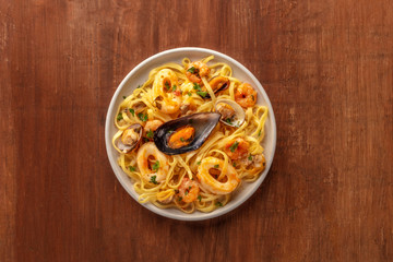 Seafood pasta. A plate of tagliolini with mussels, shrimps, clams and squid rings, shot from the top on a dark rustic wooden background with a place for text