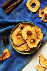 Apple chips and cinnamon on white wooden table. Homemade dry baked fruit slices, autumn fall snack, healthy vegan food. Vertical, top view, flat lay.
