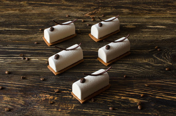 Coffee mini mousse cakes covered with white velvet spray, decorated with coffee beans and chocolate elements on a wooden table