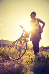 Enjoying the evening sun, sundown scenery: woman with bike is standing beside her bike, sunbeam