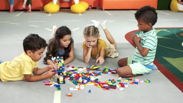 Four beautiful kids in playroom. Colorful blocks on the floor. Kids playing with constructor toys in kindergarten, playschool or daycare center.