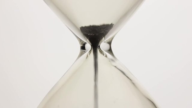 Close-up of black magnetic powder flowing through a hourglass on white background