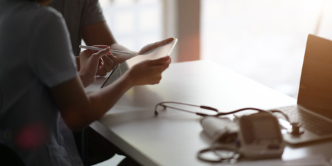 Asian woman doctor with tablet talking to male Asian patient in office